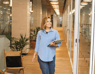 A smiling businesswoman walking down an office corridor with a tablet