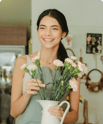 Une fleuriste souriante tenant un pichet d’œillets
