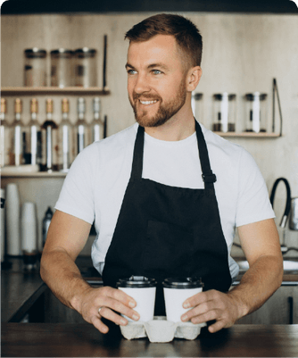 A café owner behind the counter holding a tray of coffees