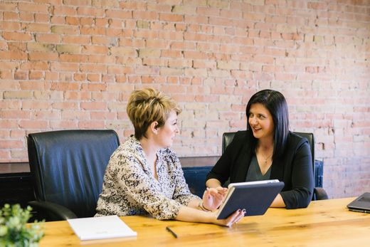 Two women reviewing documents on a tablet at a meeting table